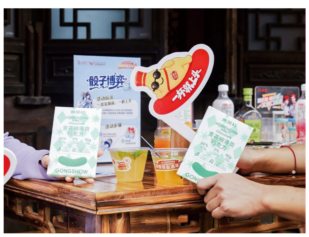 活动现场桌面摆放两盒青花椒薄荷巧克力和饮品，参与者手持产品展示